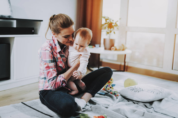 Young Mother Playing Toys with Cute Baby on Carpet. Smiling Mom Wears Casual Clothes Holding Sweet Beautiful Caucasian Toddler on Knees and Sitting near Large Panoramic Window in Living Room. - Foto, Bild