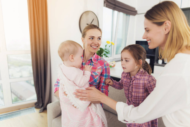 Babysitter and Mother Play with Children Indoors. Smiling Caucasian Happy Nanny Holding Baby on Hands and Businesswoman Mom and Daughter Hugging Child in Bright Living Room. - Foto, Imagen