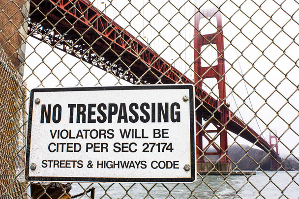 A 'No Trespassing' sign in Fort Point, with the Golden Gate Bridge in the background - Photo, Image