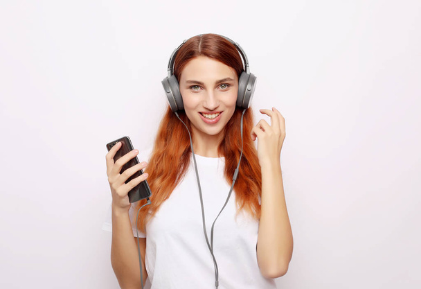 Beautiful young woman in headphones listening to music on white background - Valokuva, kuva