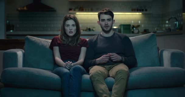 Koppel op een sofa thuis reageren op een schokkend moment op tv - Video