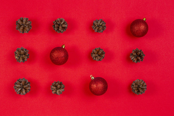 Weihnachtskomposition. Muster aus Tannenzapfen und roter Weihnachtsdekoration auf rotem Hintergrund. Draufsicht, flache Lage - Foto, Bild