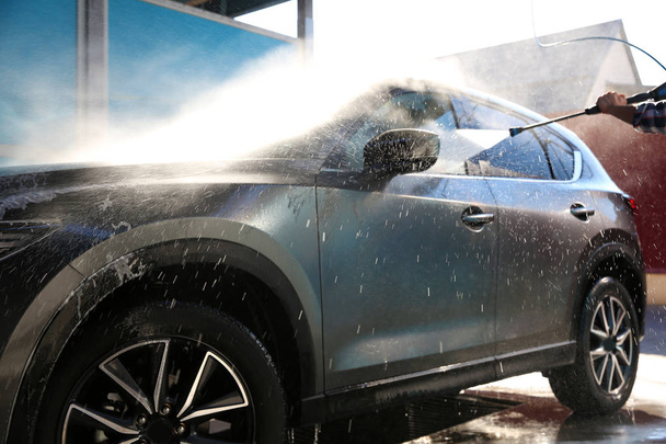 Worker cleaning automobile with high pressure water jet at car wash - Valokuva, kuva