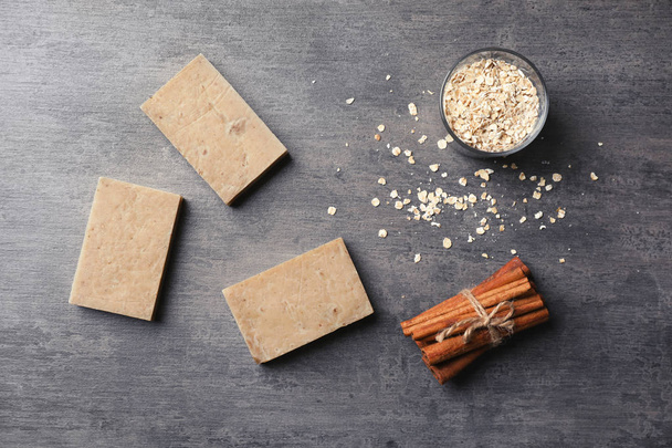 Handmade soap bars, oatmeal and cinnamon sticks on grey background, top view - Fotó, kép