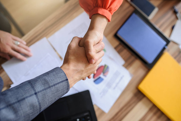 Een zakenvrouw en een man op een houten kantoor bureau handshaking, alleen handen, grijze achtergrond - Foto, afbeelding