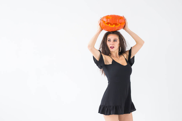 Portrait of a stylish brunette woman with halloween pumpkin over light background with copy space - Valokuva, kuva