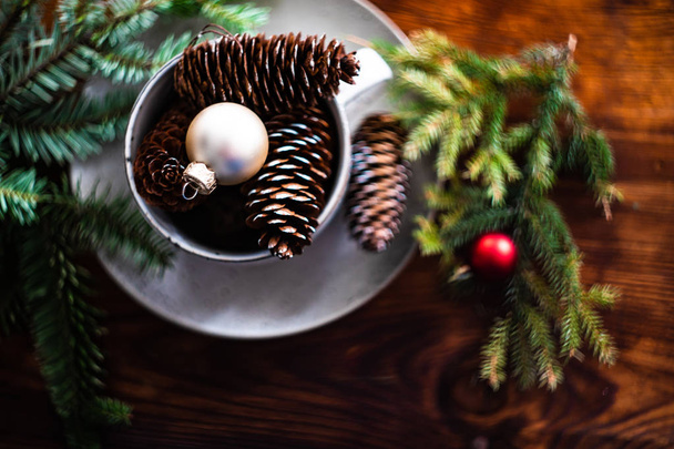 Festive table setting with ceramic plate and cup full of pine cones and decor on wooden background - Фото, зображення