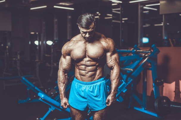 Handsome young fit muscular caucasian man of model appearance workout training in the gym gaining weight pumping up muscle, poses, drinks water  fitness and bodybuilding sport nutrition concept - 写真・画像