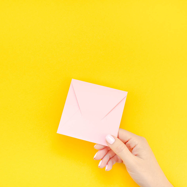 大胆な黄色の背景の創造的なミニマル スタイルにコピー スペースを持つ小さな愛千年ピンク手紙を保持パステル カラーのマニキュアで女性の手。バレンタインの休日のフェミニンなブログの正方形の概念テンプレート - 写真・画像