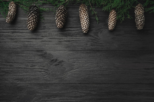 Tarjeta de Navidad. Fondo de madera negra, con ramas de abeto y conos superiores, vista superior
 - Foto, imagen