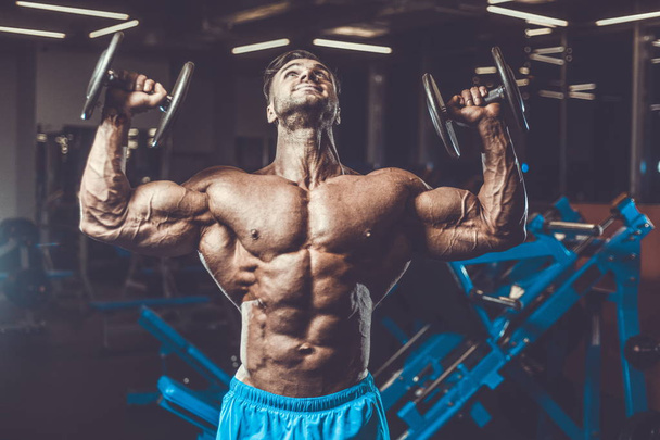 Handsome young fit muscular caucasian man of model appearance workout training in the gym gaining weight pumping up muscle, poses, drinks water  fitness and bodybuilding sport nutrition concept - 写真・画像