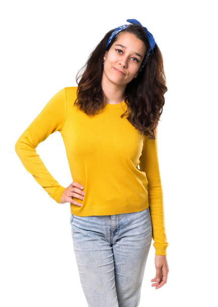 Menina com suéter amarelo e bandana azul na cabeça posando com os braços no quadril e sorrindo no fundo branco isolado
 - Foto, Imagem