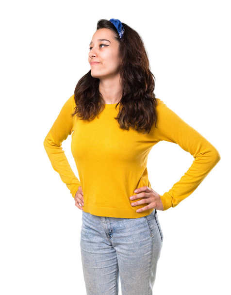 Молода дівчина з жовтим светром і блакитною банданою на голові позує руками на стегні і сміється на ізольованому білому тлі
 - Фото, зображення