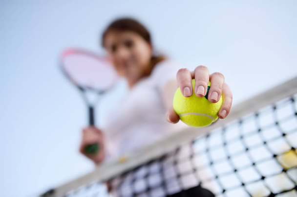 Young female tennis player with tennis ball and racket preparing to serve. Girl on tennis court. Focus on ball. - Photo, image