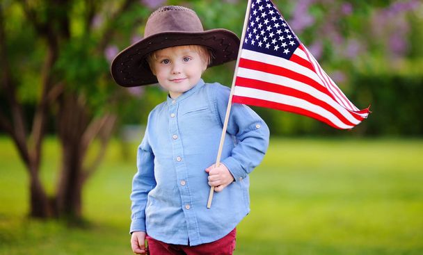 Cute toddler boy holding american flag in beautiful park. Independence Day concept. - Foto, Imagem