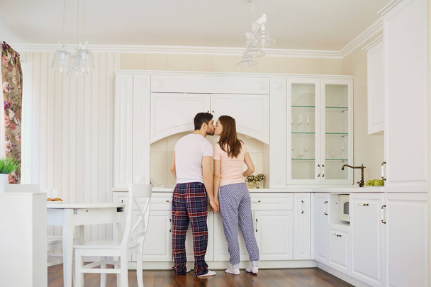 Rear view of a young couple in pajamas stand in the kitchen. - Foto, imagen