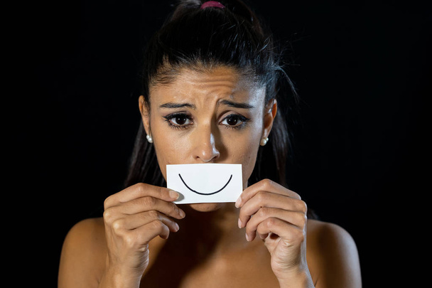 Dramatische close-up portret van triest vrouw haar depressie verbergen met glimlach geschilderd op papier in menselijke emotie lijden in stilte depressie concept geïsoleerd op zwarte achtergrond. - Foto, afbeelding