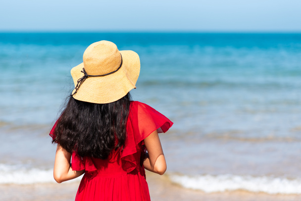 Woman walking by the seaside wearing red dress on a sunny day - Foto, Imagen