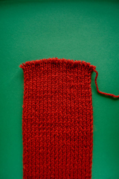 Bright red scarf with knitting needles. On green background. Green and red contrast. - Photo, Image