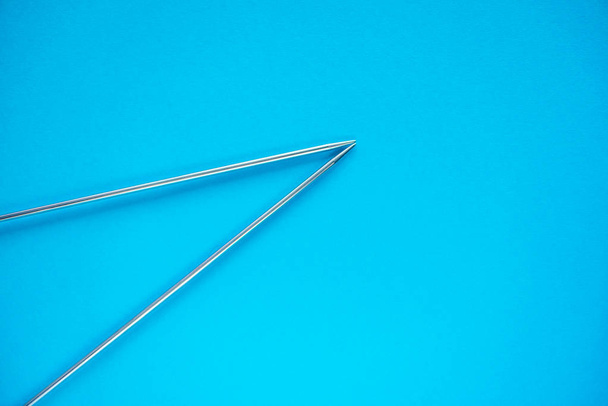 Long iron knitting needles on light blue background. - 写真・画像