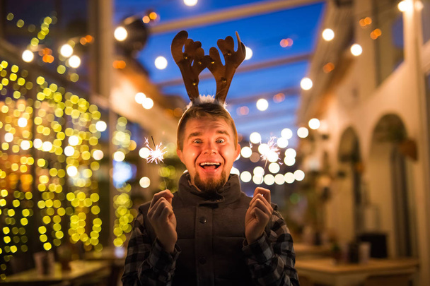 Persone, vacanze e concetto di Natale - uomo sorpreso nelle corna dei cervi che tiene due bengala luce o scintille all'aperto
 - Foto, immagini