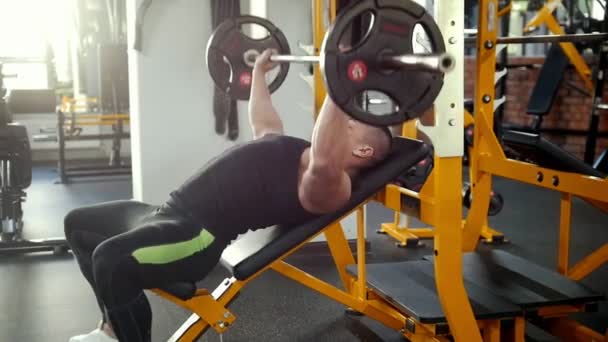 Bodybuilder performing incline barbell press exercise on a bench in the gym. - Materiaali, video