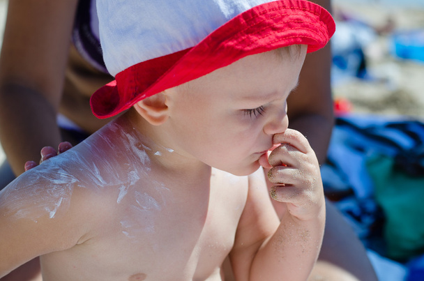 schattige kleine jongen met zonnebrandcrème toegepast - Foto, afbeelding