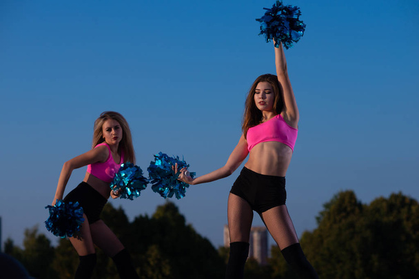 Two girls cheerleaders with pompons dancing outdoors on sky background - Fotoğraf, Görsel