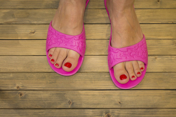 Vrouwelijke voeten in slippers op houten vloer of achtergrond - Foto, afbeelding