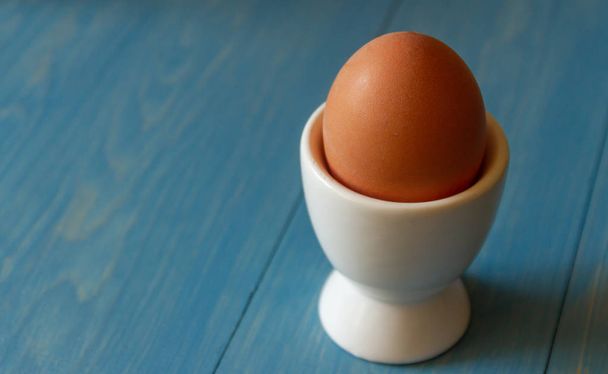 Одно сваренное яйцо в белой яйцеклетке на синем фоне
 - Фото, изображение