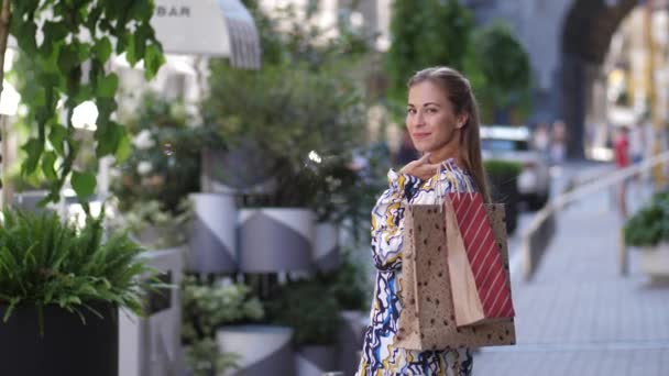 Zeitlupenporträt einer lächelnden Shopaholic-Frau, die mit Papiertüten auf der Straße läuft, sich dreht und in die Kamera schaut, Einkäufe und die Stadt genießt. 4k - Filmmaterial, Video