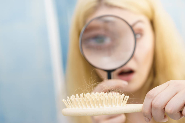 Woman using magnifying glass looking at her brush. Examing hair loss, haircare concept. - Foto, Bild