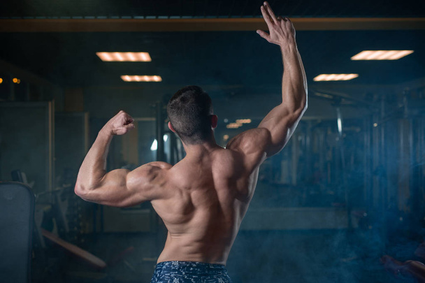 A brutal athletic man with a muscular body poses in the gym, showing off his biceps and back. The concept of a healthy lifestyle - Photo, Image