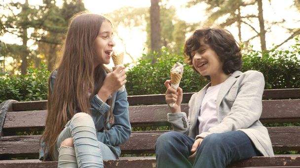 cute teenagers, boy and girl eating ice cream in the park and talking - 写真・画像