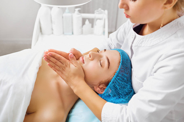 Cosmetologist makes facial massage to a young woman. - Fotoğraf, Görsel