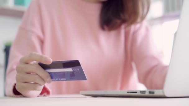 Gyönyörű ázsiai nő segítségével a számítógép vagy laptop vásárlás online vásárlás bankkártyával kopás pulóver íróasztal otthon a nappaliban ül míg. Életmód nő a haza fogalma. - Felvétel, videó