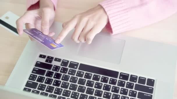 Азиатская женщина, пользуясь компьютером или ноутбуком, совершает онлайн-покупки с помощью кредитной карты, а свитер носит сидя дома на столе в гостиной. Концепция "женщина дома"
. - Кадры, видео