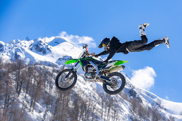 kilpailija moottoripyörällä lennon aikana, hyppää ja lähtee ponnahduslauta vastaan lumiset vuoret
 - Valokuva, kuva