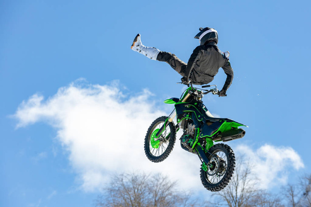 гонщик на мотоциклі в польоті, стрибає і злітає на трампліні проти засніжених гір
 - Фото, зображення