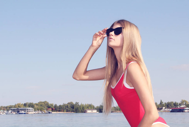 Menina loira bonita com cabelos longos em óculos de sol e maiô vermelho
. - Foto, Imagem