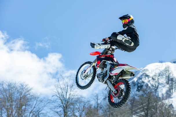 Racer op een motorfiets tijdens de vlucht, springt en neemt af op een springplank tegen de besneeuwde bergen. Concept actieve extreme rust. lichtstraal - Foto, afbeelding