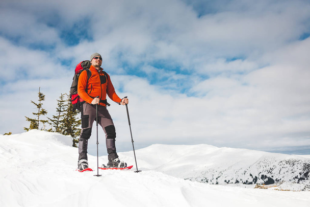 Winter beklimming van de berg. Een man in sneeuwschoenen is klimmen naar de top. Winterbeklimming. Een bergbeklimmer met een rugzak en trekking stokken. Apparatuur voor Winterwandelen. - Foto, afbeelding