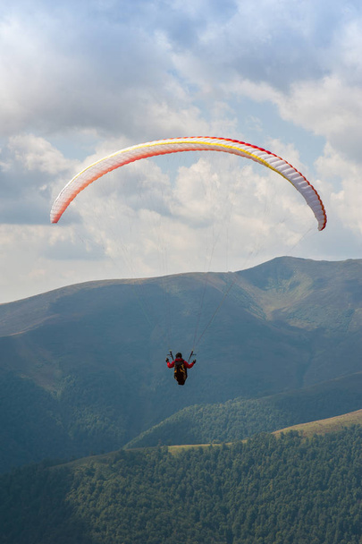 Um parapente voa sobre um vale de montanha em um dia ensolarado de verão. Parapente nos Cárpatos no verão
. - Foto, Imagem