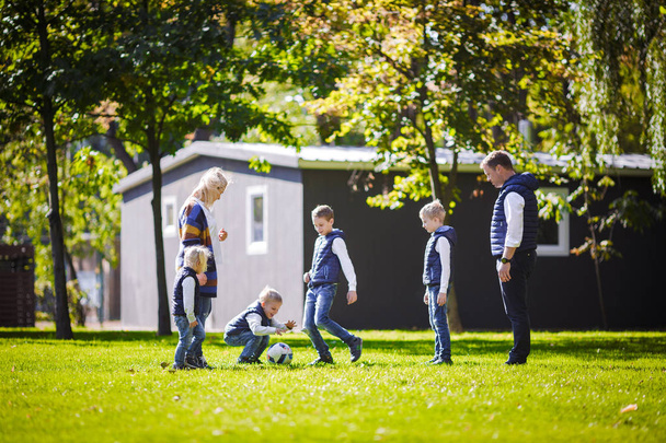 Teema perheen ulkoilu. Iso ystävällinen valkoihoinen perhe kuusi äiti isä ja neljä lasta pelaa jalkapalloa, käynnissä pallo nurmikolla, vihreä ruoho nurmikko lähellä taloa aurinkoisena päivänä
. - Valokuva, kuva