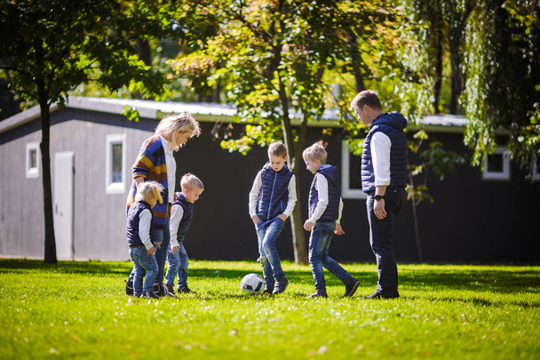 das Thema Familie Outdoor-Aktivitäten. große freundliche kaukasische Familie mit sechs Mamas Papa und vier Kindern beim Fußballspielen, Laufen mit dem Ball auf dem Rasen, grüne Rasenfläche in der Nähe des Hauses an einem sonnigen Tag. - Foto, Bild