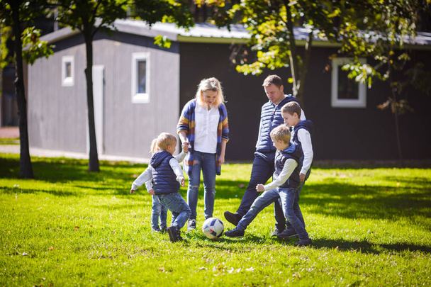 テーマ家族の屋外活動。フレンドリーな白人の大家族 6 お母さんお父さんとサッカー ボールを持って、芝生の上を実行している 4 人の子供は晴れた日に家の近くの草の芝生をグリーンします。. - 写真・画像