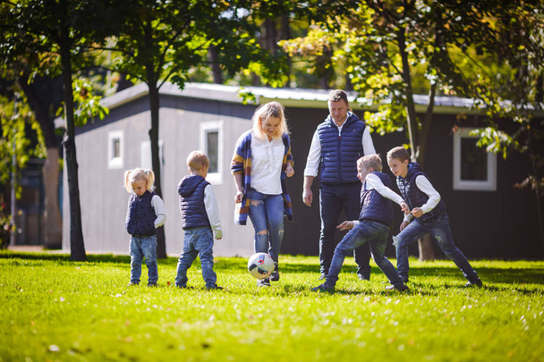 Το θέμα οικογένεια υπαίθριες δραστηριότητες. μεγάλο φιλικό οικογένεια Καυκάσιος έξι μαμά μπαμπά και τα τέσσερα παιδιά παίζει ποδόσφαιρο, τρέξιμο με τη σφαίρα στο γρασίδι, πράσινο γρασίδι κοντά στο σπίτι σε μια ηλιόλουστη ημέρα. - Φωτογραφία, εικόνα