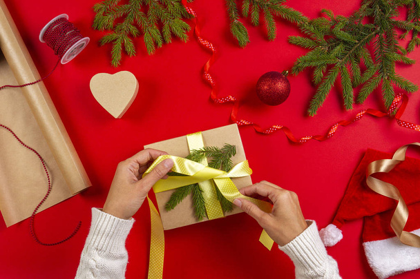 Christmas gift wrapping. Womans hands packing Christmas present box on red table background - Photo, Image