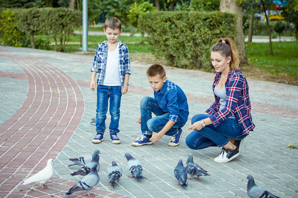 Young beautiful mother and her two sons enjoying together fed pigeons. Happy family. Positive human emotions, feelings, joy. - Photo, Image