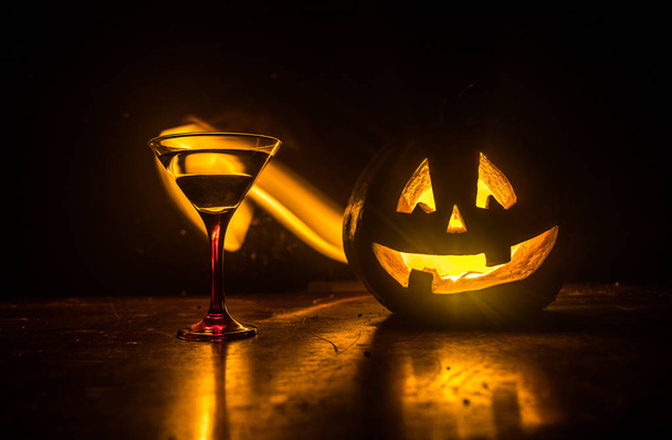 Halloween pumpkin orange cocktails. Festive drink. Halloween party. Funny Pumpkin with a glowing cocktail glass on a dark toned foggy background. Selective focus - Photo, Image